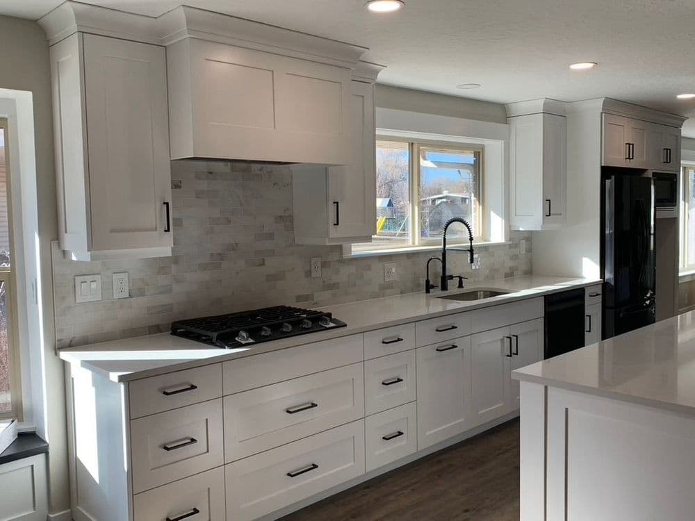 Modern kitchen with white cabinets, marble backsplash, gas stove, and large windows for natural light.